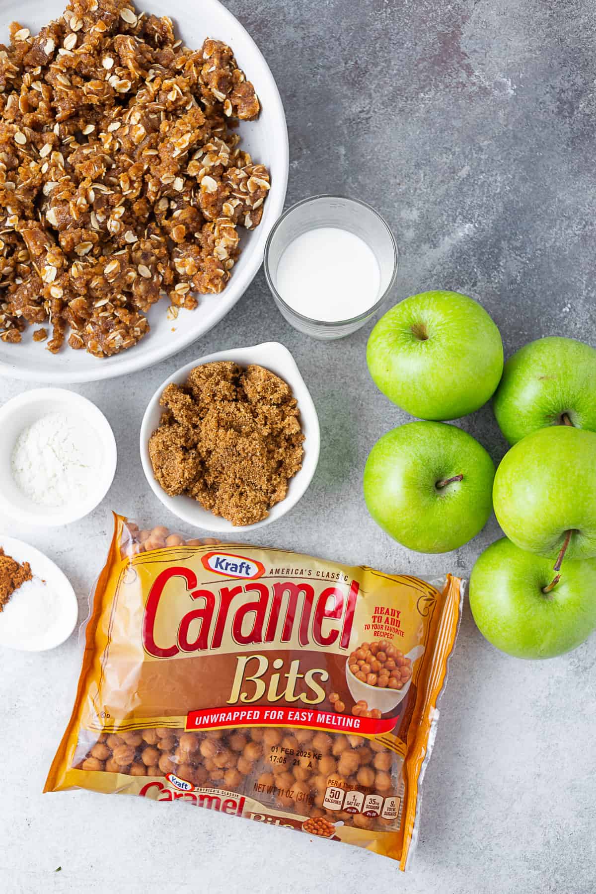 A table with crumb topping, brown sugar, flour, spices, and caramel bits sitting on it. 