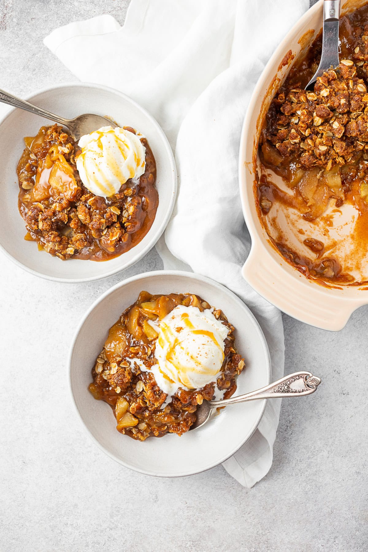 Two bowls filled with caramel apple crisp and topped with ice cream. 