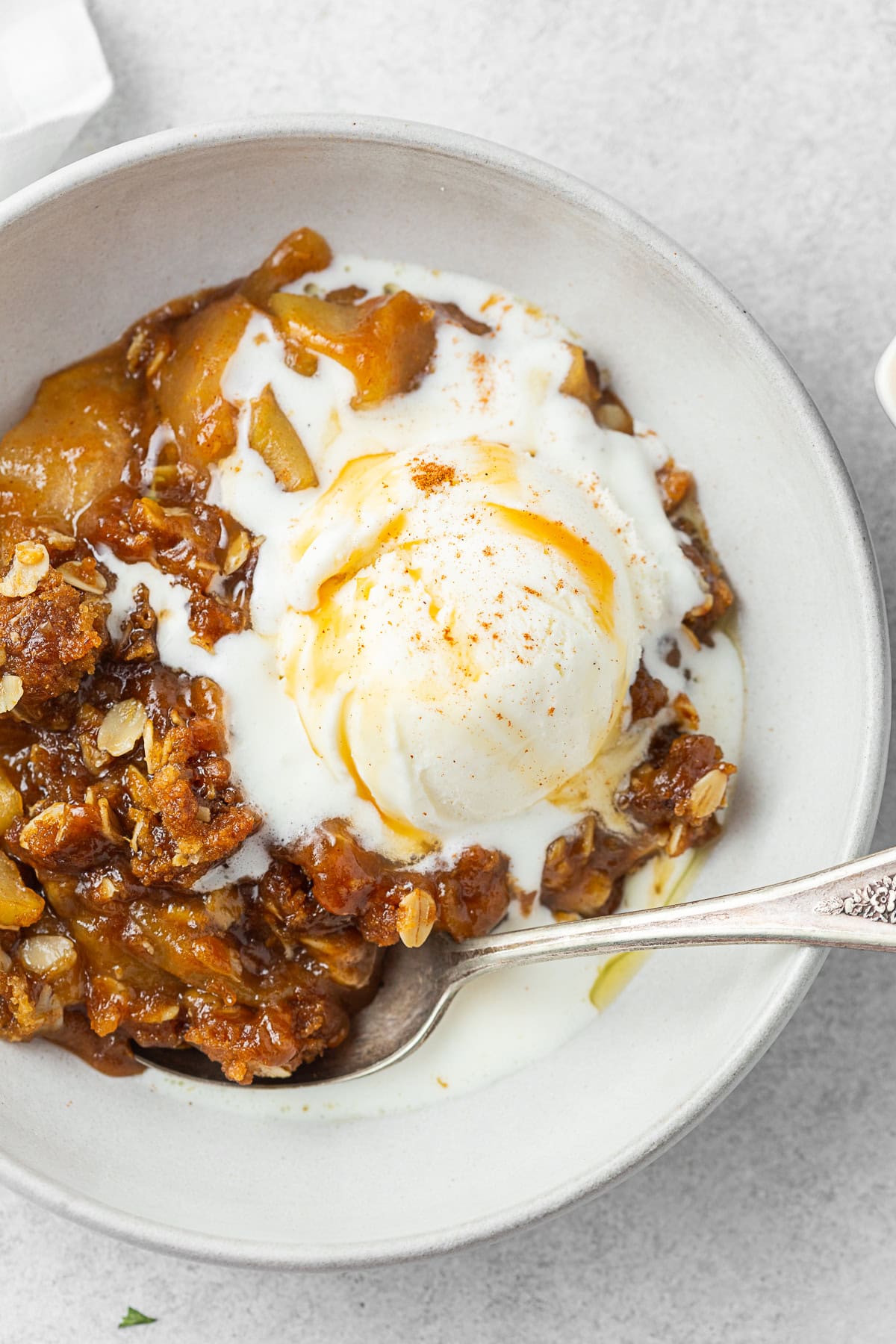 Easy caramel apple crisp in a bowl with a spoon and melted vanilla ice cream. 