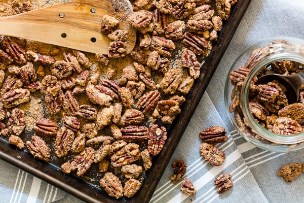 Praline Pecans on a sheet pan getting put into a gift jar.