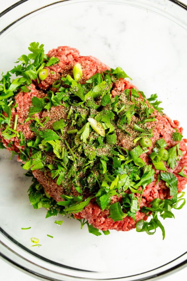 Ground beef, chopped parsley, and green onions in a bowl. 