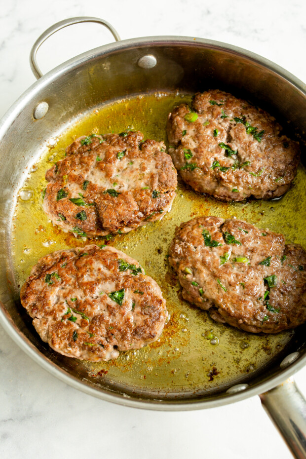 Salisbury steak pan frying in a large skillet. 