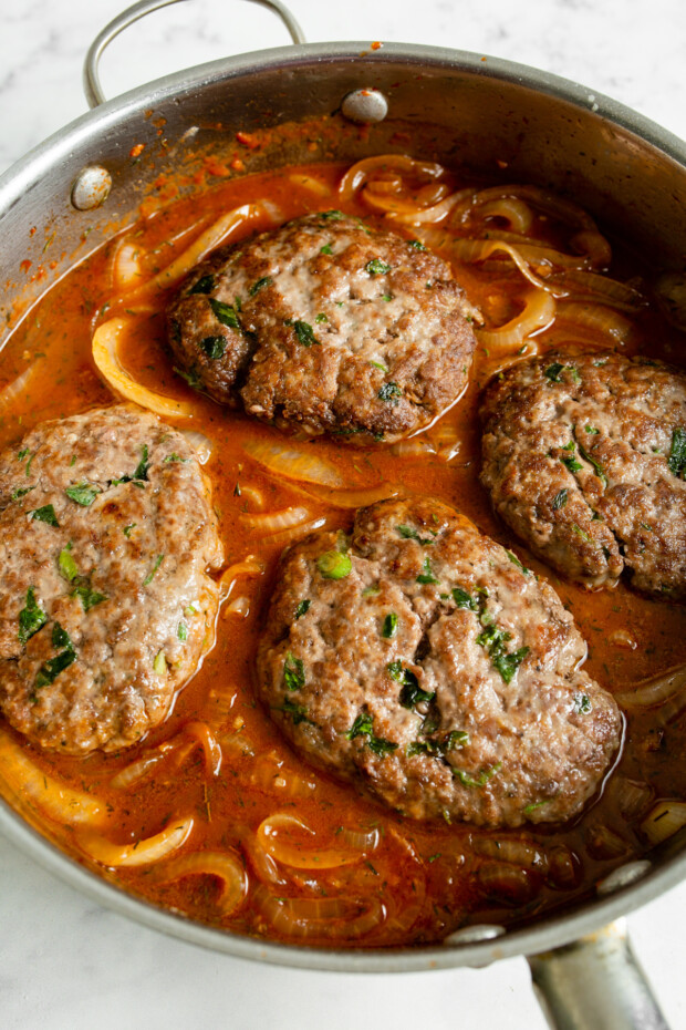 French Onion Salisbury Steak cooking in a large skillet. 