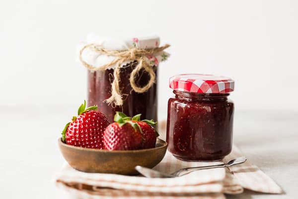 2 jars of vanilla bean strawberry jam with a little plate of straawberries