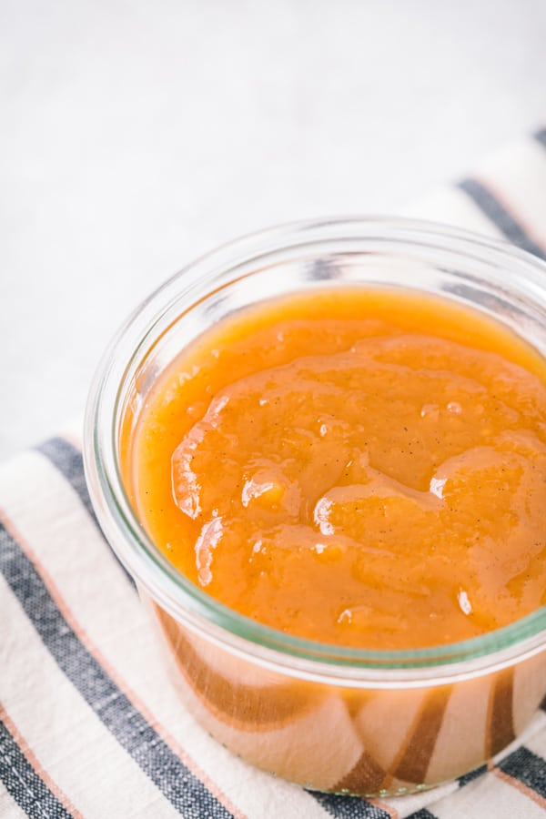 A jar filled with vanilla honey peach butter on a striped napkin.
