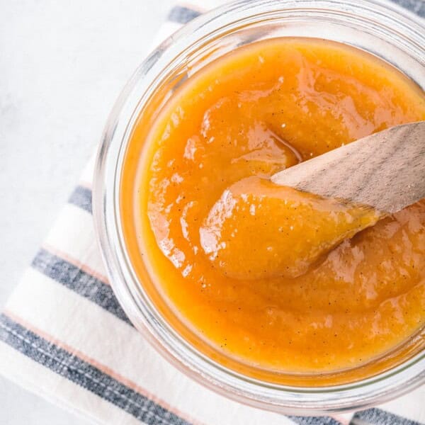 vanilla honey peach butter in a glass jar with a wooden knife