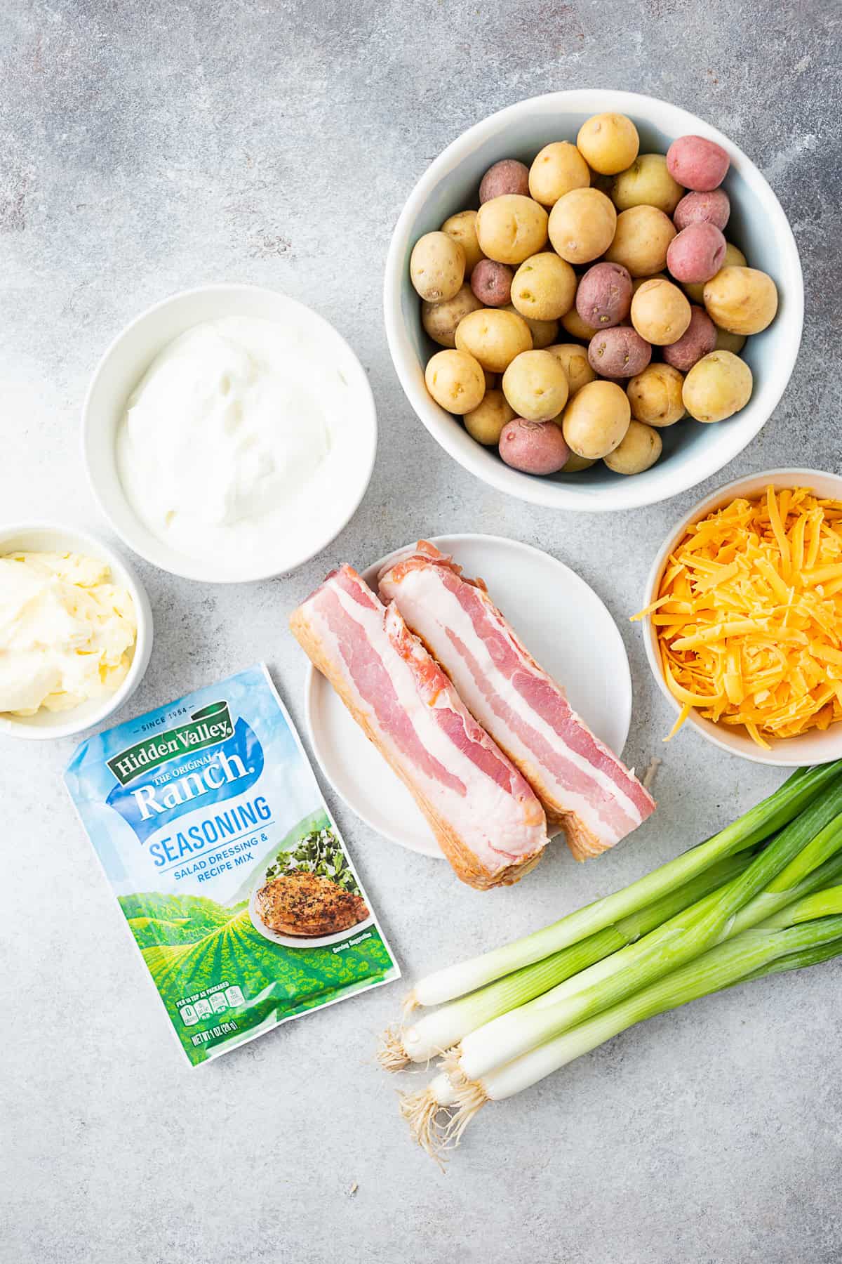 Bacon Ranch Potato Salad by Nutmeg Nanny Bacon, potatoes, cheese, onions, sour cream, mayonnaise, and Ranch seasoning on a table.
