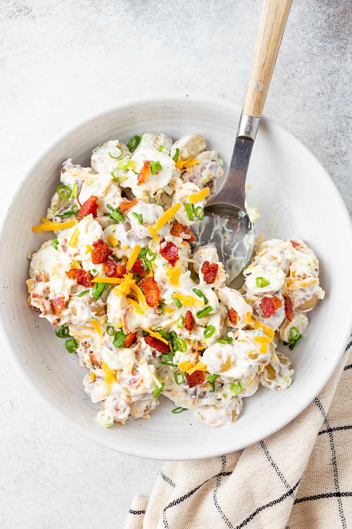 Bacon Ranch Potato Salad by Nutmeg Nanny Bacon Ranch Potato Salad in a white bowl with a serving spoon.