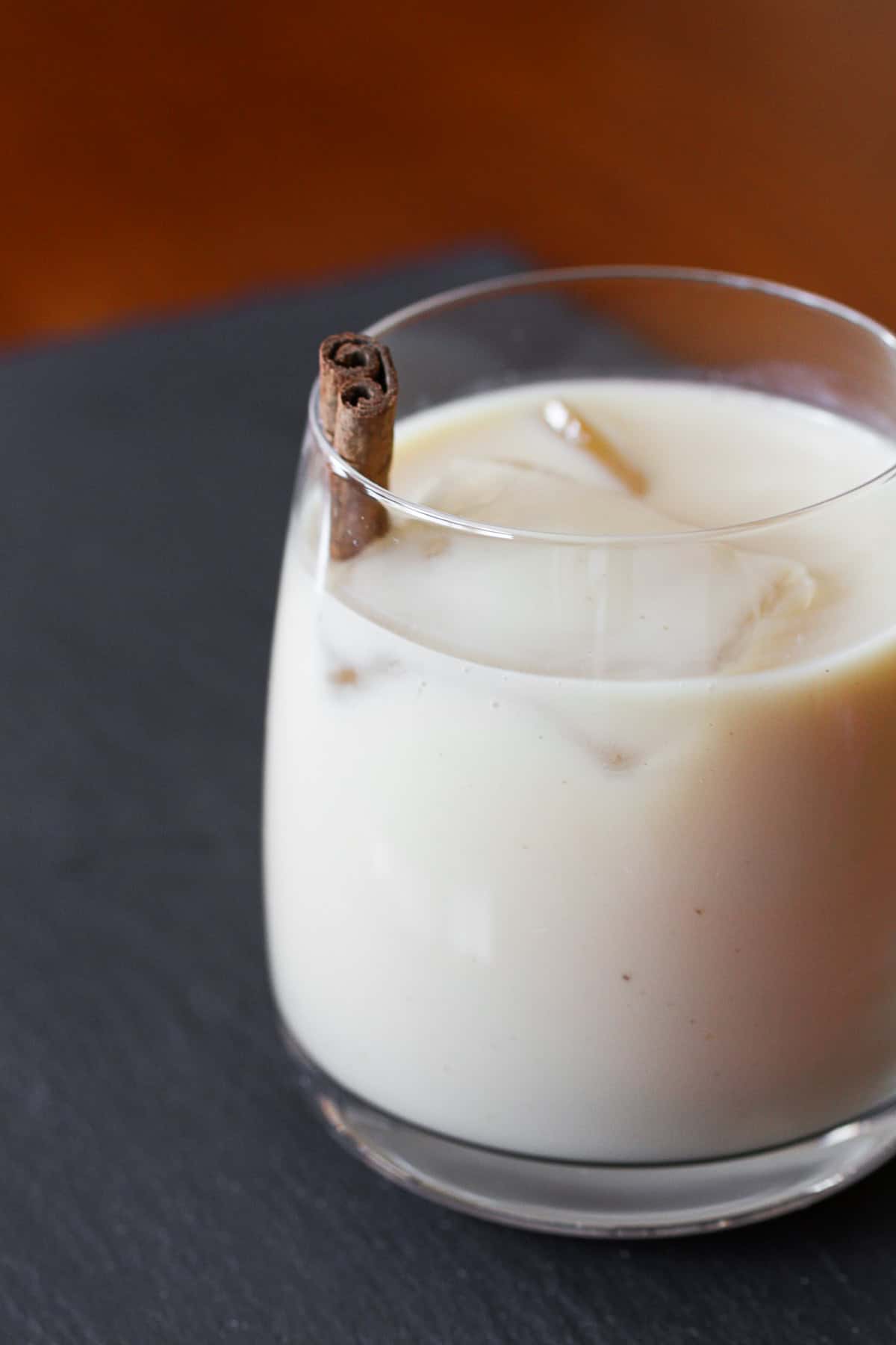 Coquito by Nutmeg Nanny {The Twelve Boozy Days of Christmas} Coquito in a glass with a cinnamon stick.