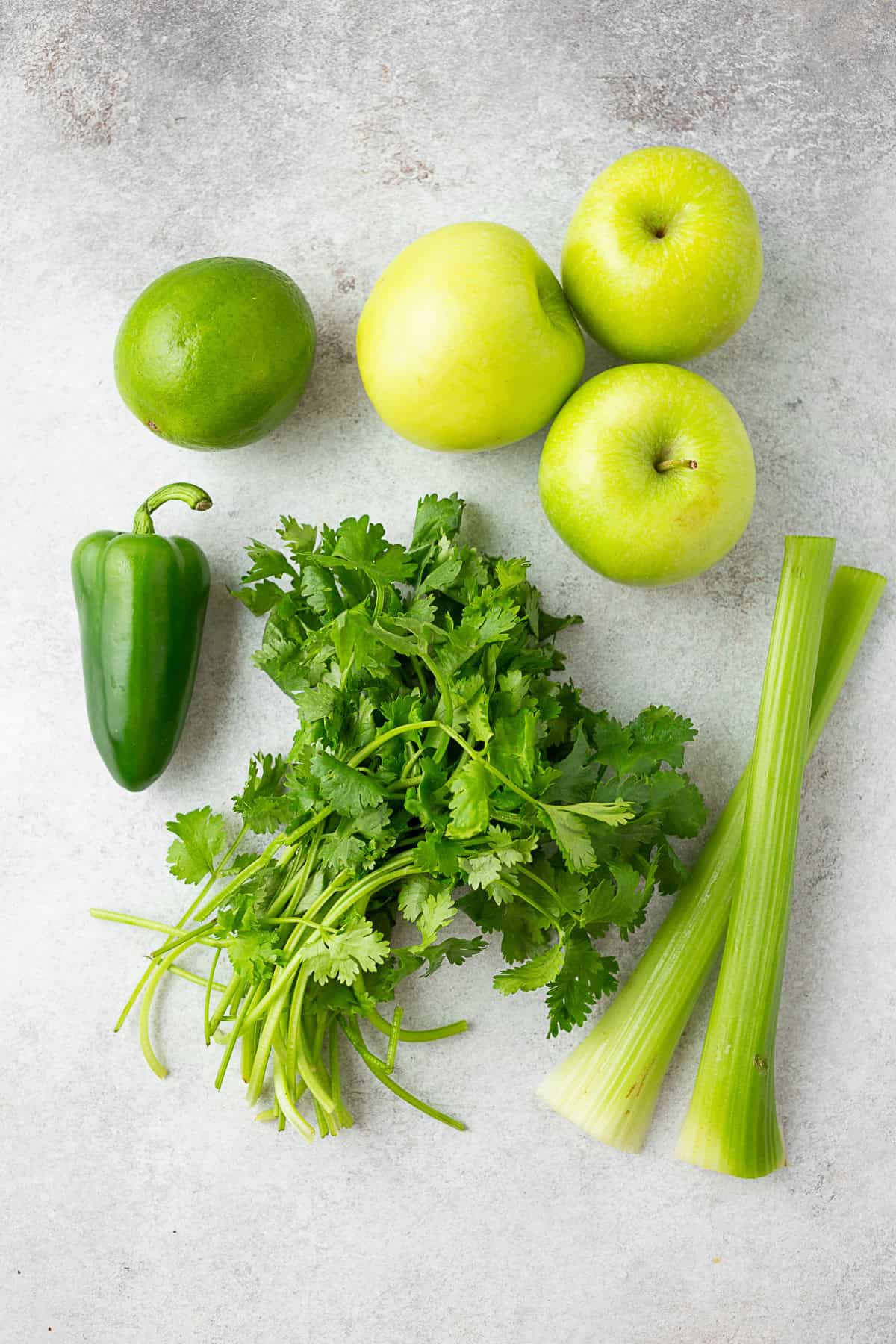 Celery, cilantro, apple, jalaepno, and lime on a table. 
