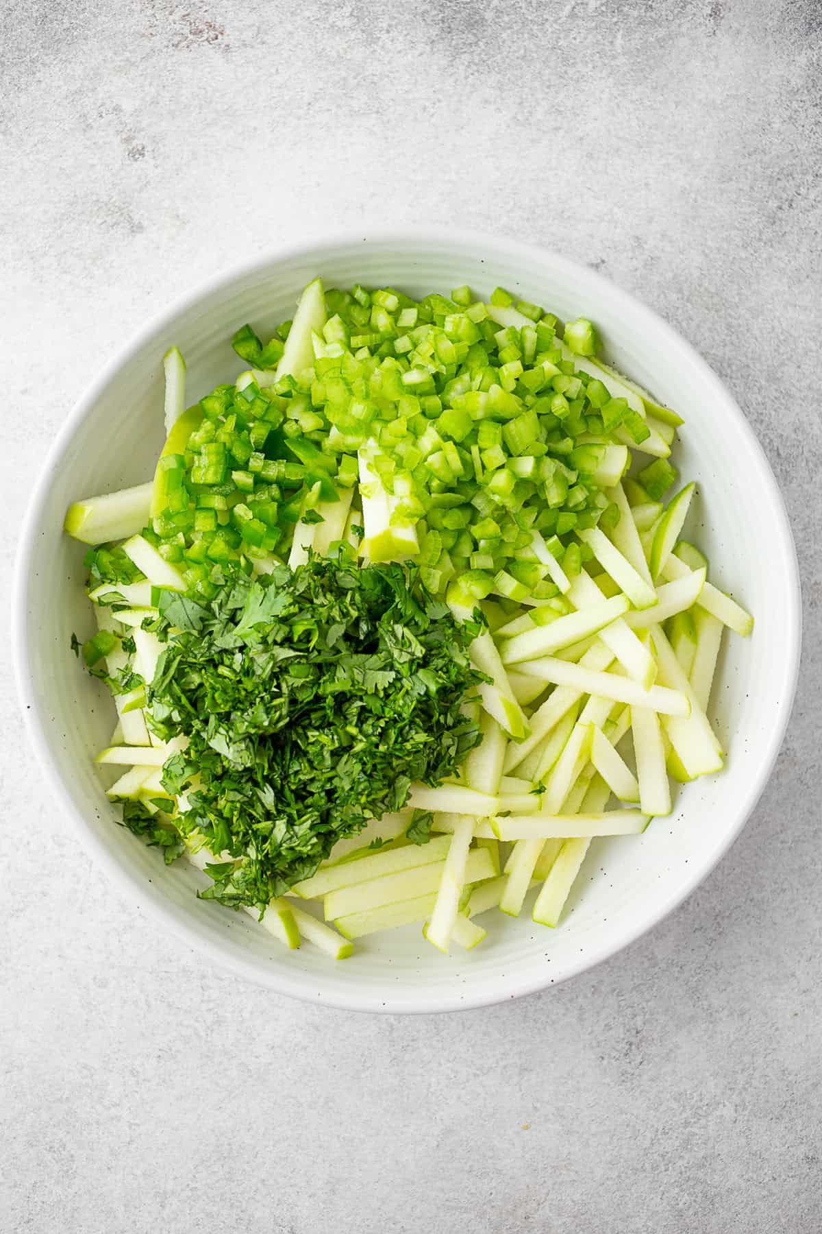 Matchstick cut apples with cilantro, jalapeno, and celery in a bowl. 