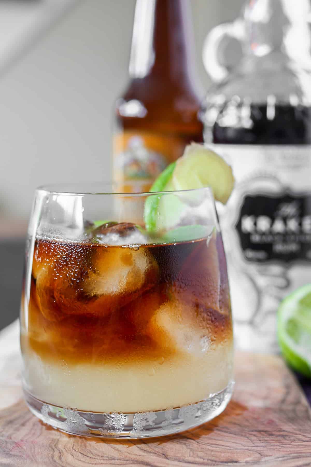 Dark and Stormy Cocktail in a glass on a table with rum bottle in the background. 
