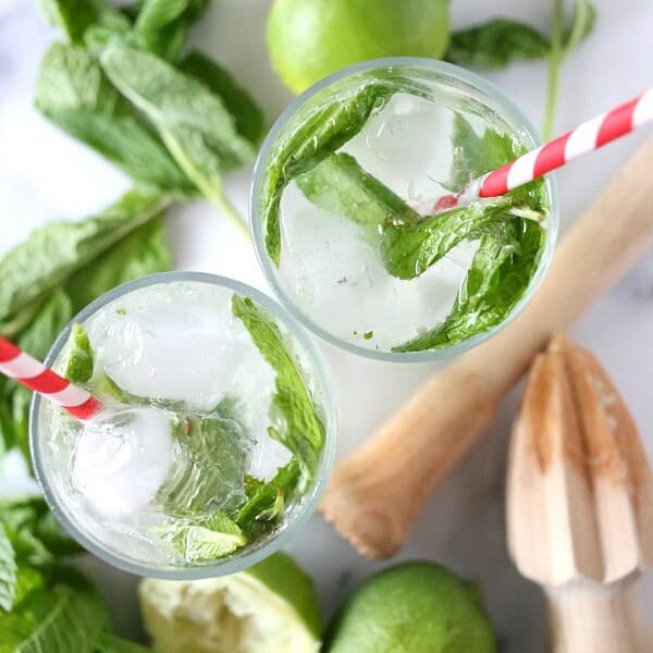 coconut mojitos in a tall cocktail glass surrounded by fresh mint and limes