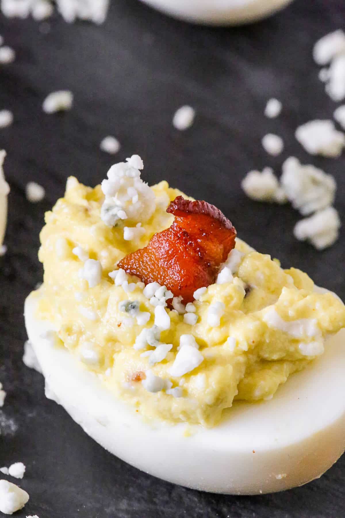 Blue Cheese Deviled Eggs on a slate plate with a piece of bacon on top. 