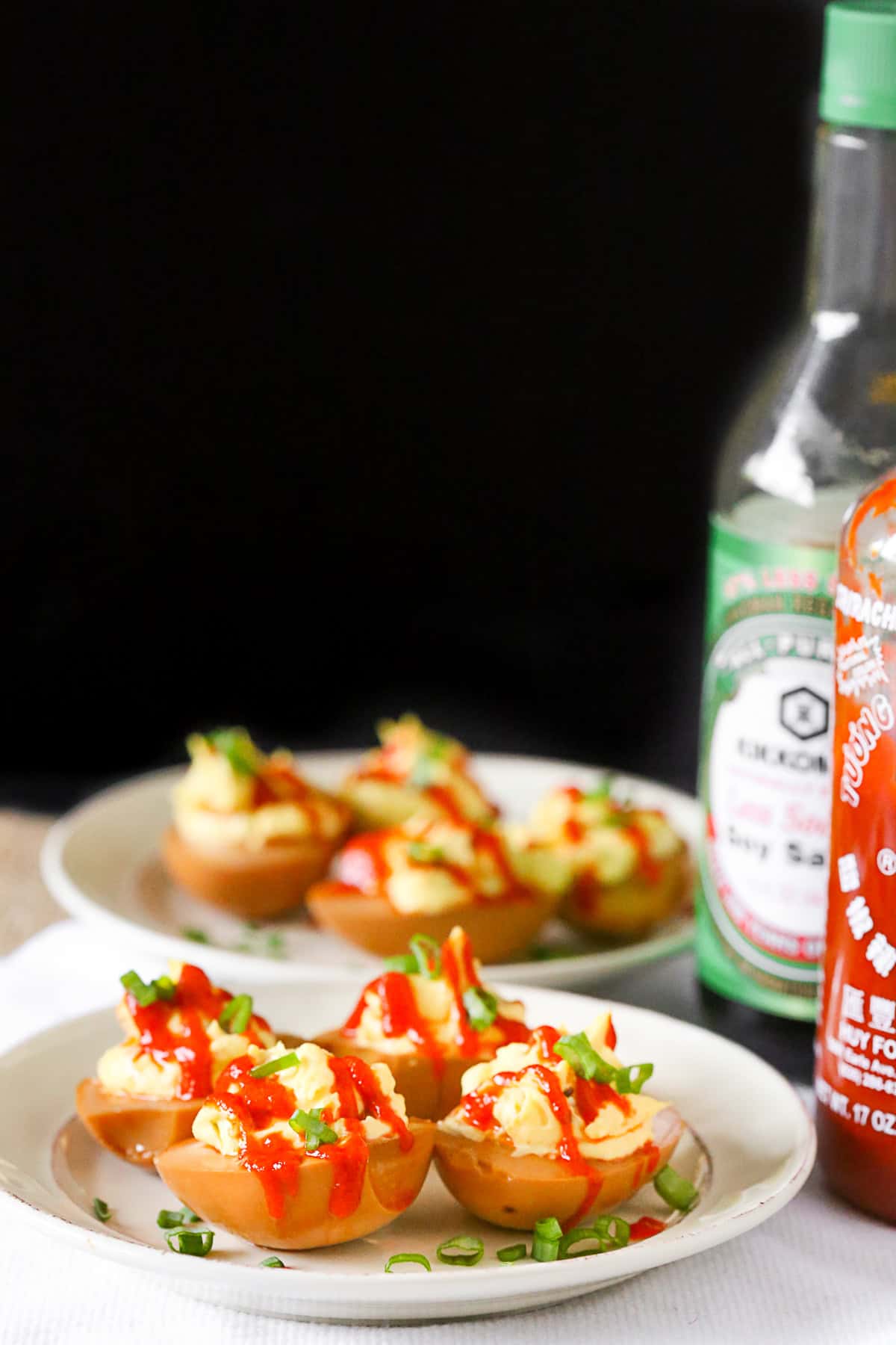Soy Sauce Deviled Eggs on a white plate with bottle of soy sauce and sriracha next to it. 