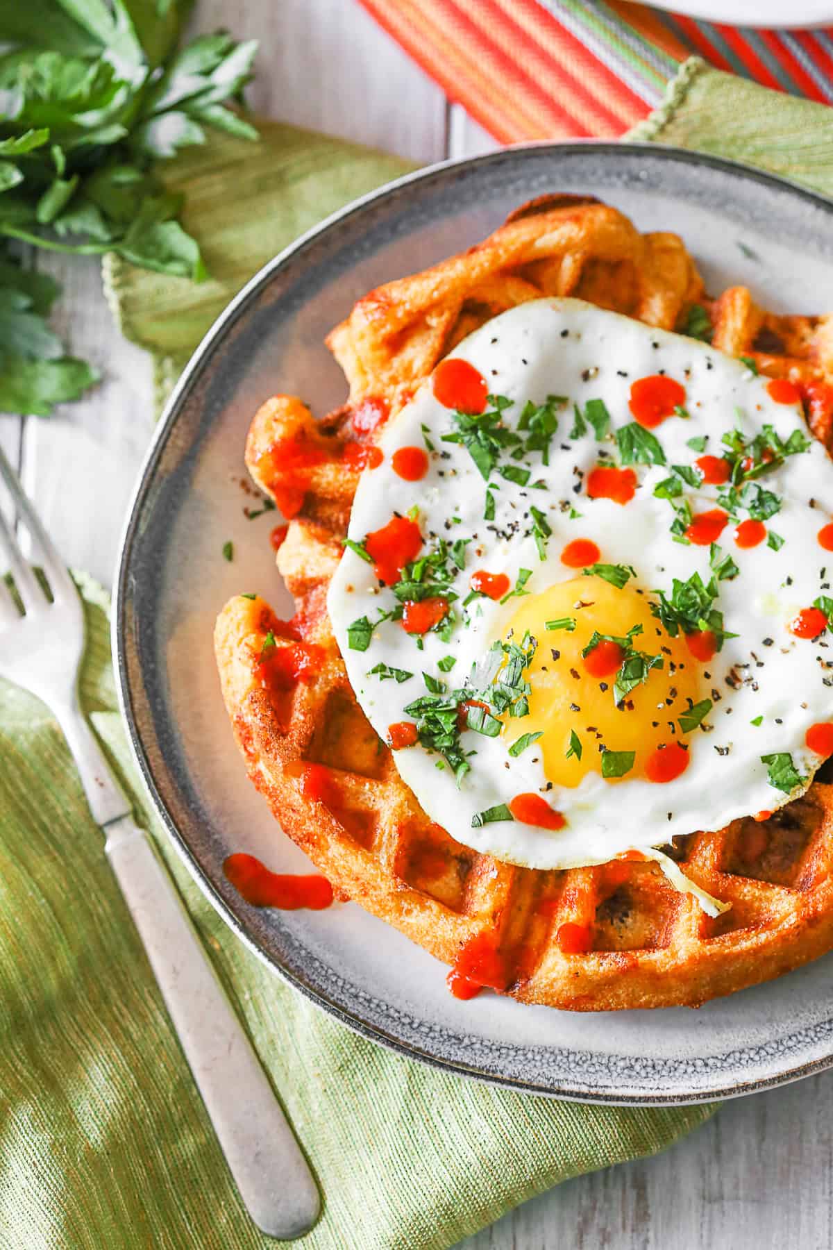 Cheddar Sausage Cornmeal Waffles topped with cilantro and sriracha. 