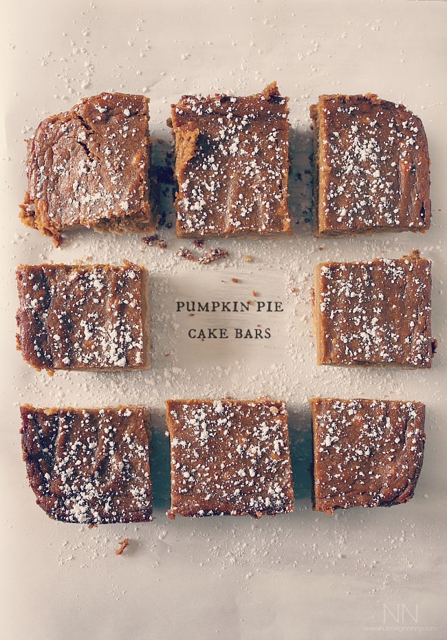 These pumpkin pie cake bars are like two desserts in one. Cake like bottom topped with a moist pumpkin pie top sprinkled with powdered sugar. Perfect for Thanksgiving! Pumpkin Pie Cake Bars cut on parchment paper.