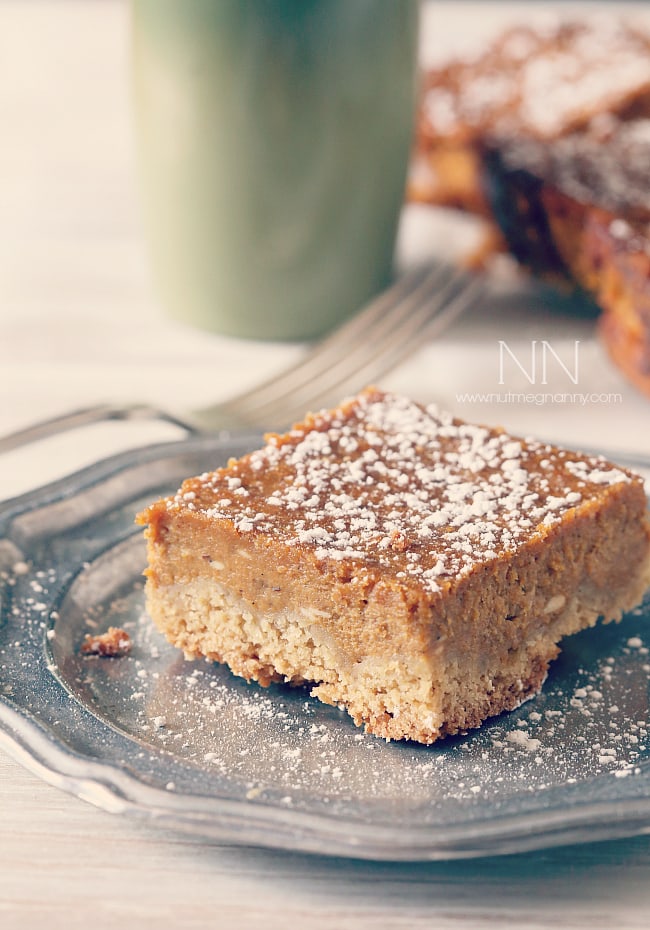 These pumpkin pie cake bars are like two desserts in one. Cake like bottom topped with a moist pumpkin pie top sprinkled with powdered sugar. Perfect for Thanksgiving! Pumpkin Pie Cake Bars sliced on a plate.