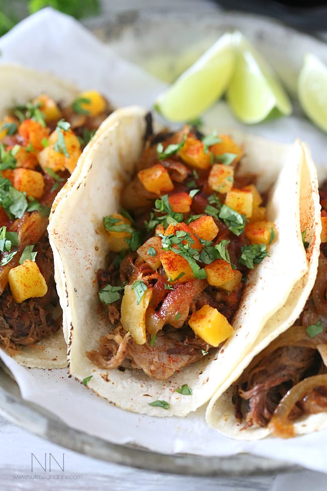 Close up of carnitas in tortillas, topped with onions, butternut squash, spices, and cilantro.