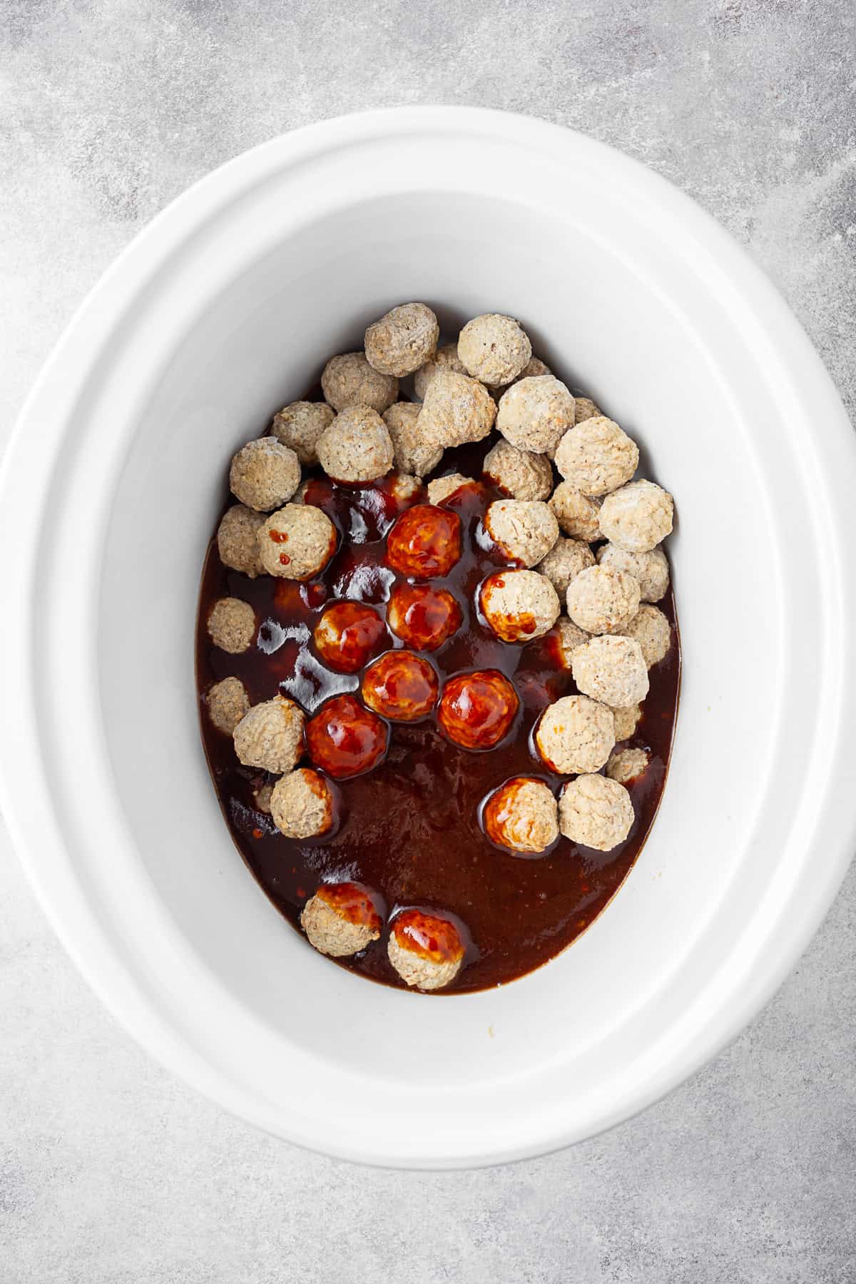 Frozen meatballs in a slow cooker crock with bbq sauce poured over them. 