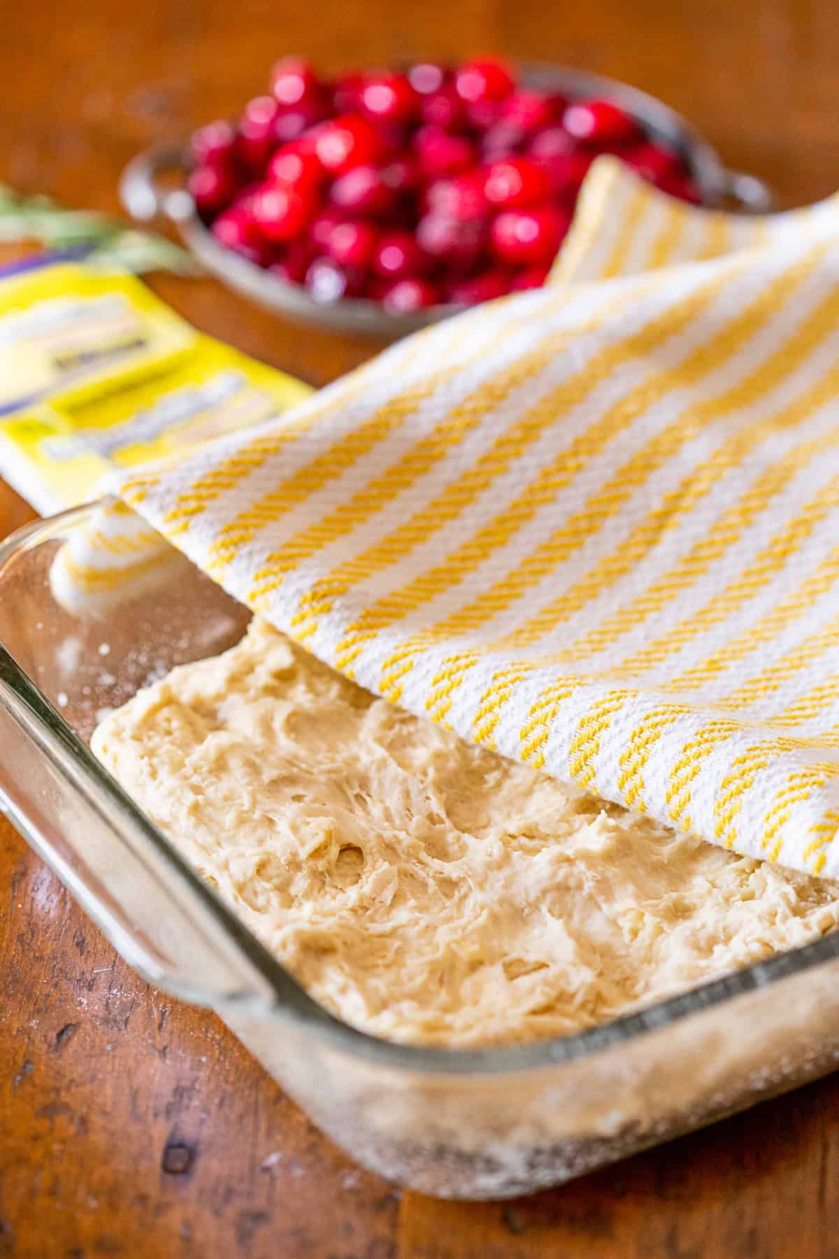 This cranberry rosemary focaccia is easily made from a fresh yeast dough and topped with lots of chopped rosemary, fresh tart cranberries and a sprinkling of kosher salt. A towel covering Cranberry Rosemary Focaccia dough.