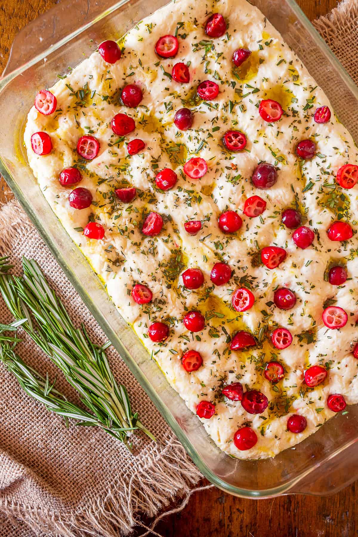 This cranberry rosemary focaccia is easily made from a fresh yeast dough and topped with lots of chopped rosemary, fresh tart cranberries and a sprinkling of kosher salt. uncooked Cranberry Rosemary Focaccia.