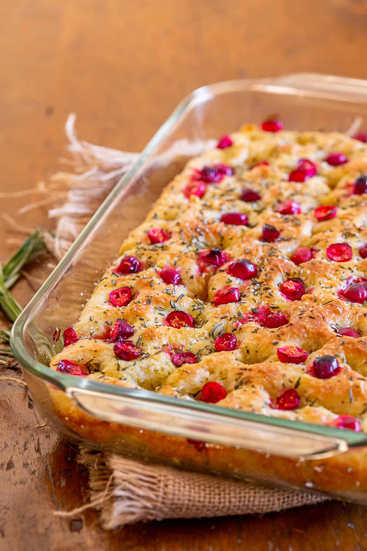 This cranberry rosemary focaccia is easily made from a fresh yeast dough and topped with lots of chopped rosemary, fresh tart cranberries and a sprinkling of kosher salt. Cranberry Rosemary Focaccia in a glass dish.