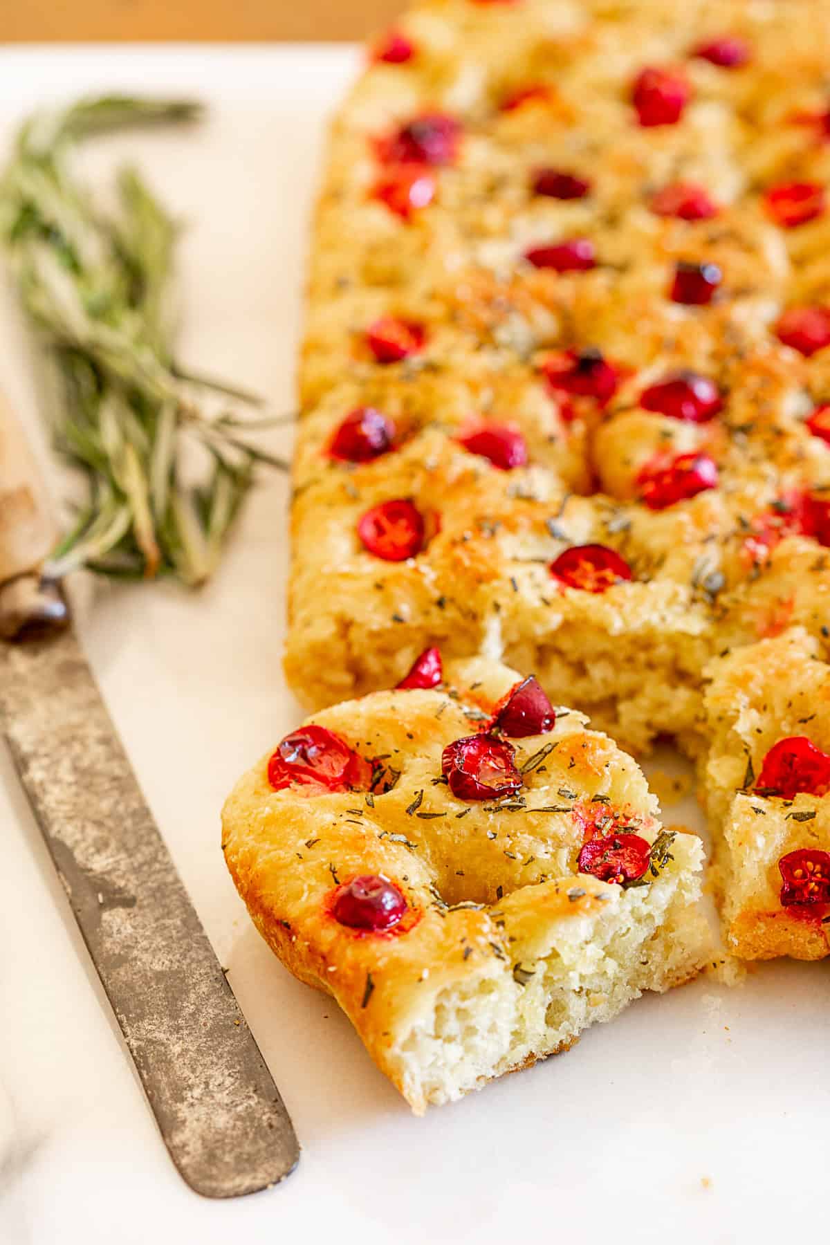 This cranberry rosemary focaccia is easily made from a fresh yeast dough and topped with lots of chopped rosemary, fresh tart cranberries and a sprinkling of kosher salt. Cranberry Rosemary Focaccia sliced on a marble tray.