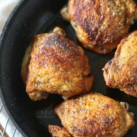 crispy pan roasted chicken thighs in a skillet sprinkled with kosher salt