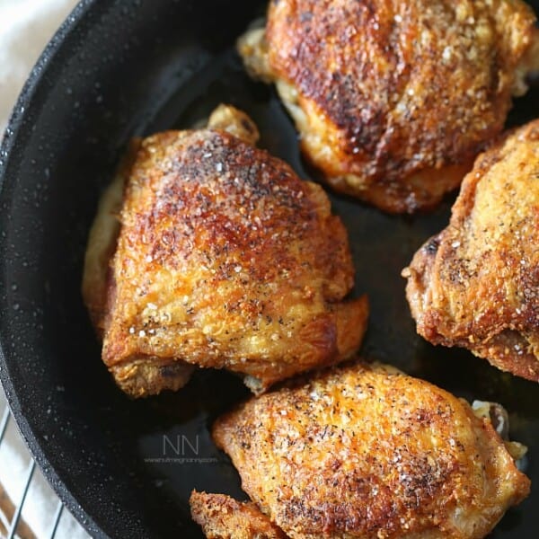 crispy pan roasted chicken thighs in a skillet sprinkled with kosher salt
