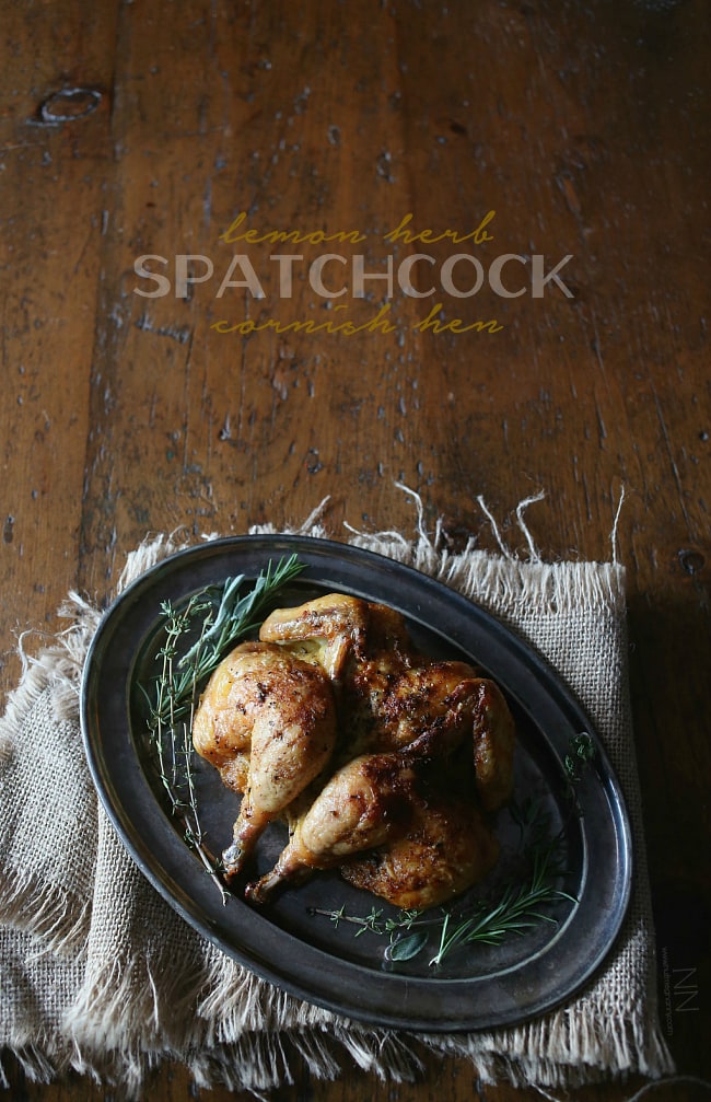 This lemon herb spatchcock Cornish hen is the perfect way to evenly cook Cornish hens. Simply cut, lay flat and rub with lemon herb butter. Hello dinner! Lemon Herb Spatchcock Cornish Hen sitting on a metal serving tray.