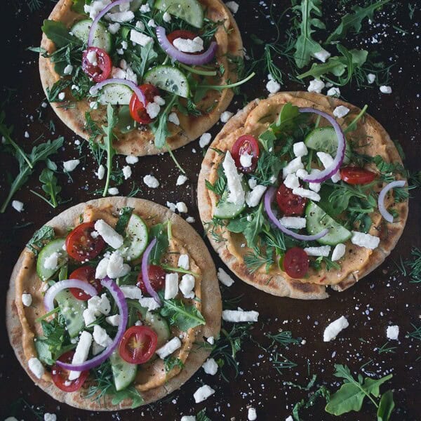 These greek salad hummus pita pizzas are the perfect summertime appetizer or main course meal. Olive oil grilled pita topped with spicy hummus and fresh Greek salad. You're going to love this!