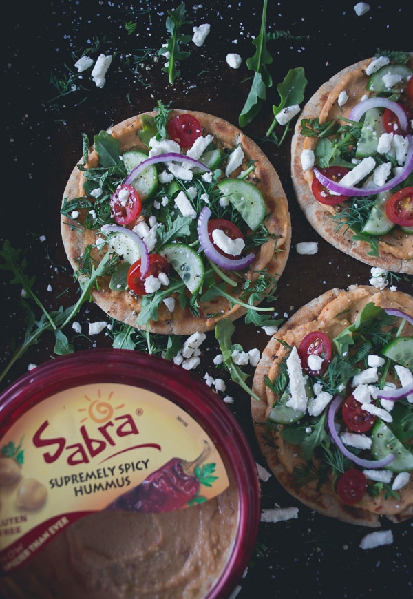 These greek salad hummus pita pizzas are the perfect summertime appetizer or main course meal. Olive oil grilled pita topped with spicy hummus and fresh Greek salad. You're going to love this!