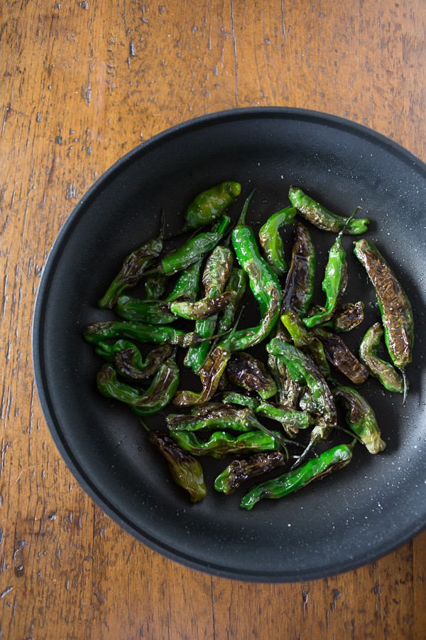 Blistered shishito peppers in a skillet.