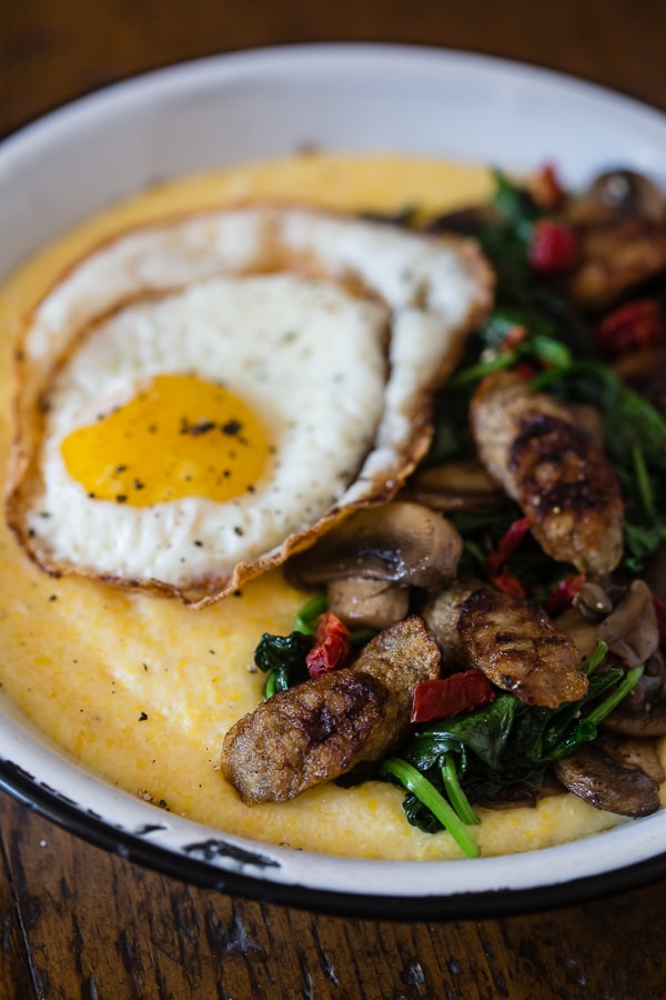 This cheesy polenta sausage breakfast bowl is packed with flavor. It starts with cheesy polenta topped with spinach, mushrooms, sun dried tomatoes, chicken sausage and topped with a crispy fried egg. Never skip breakfast again!