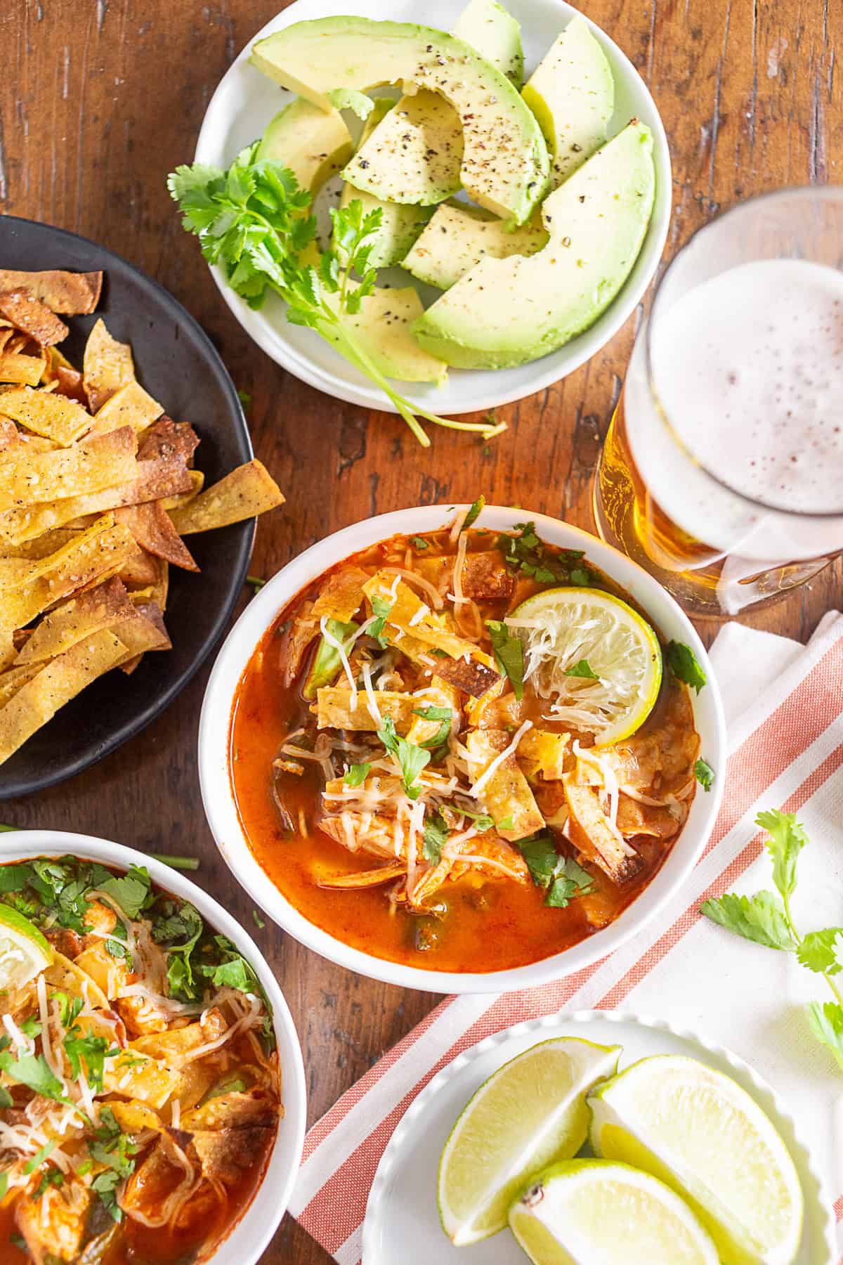 chicken and chard tortilla soup in a bowl surrounded by toppings and a beer