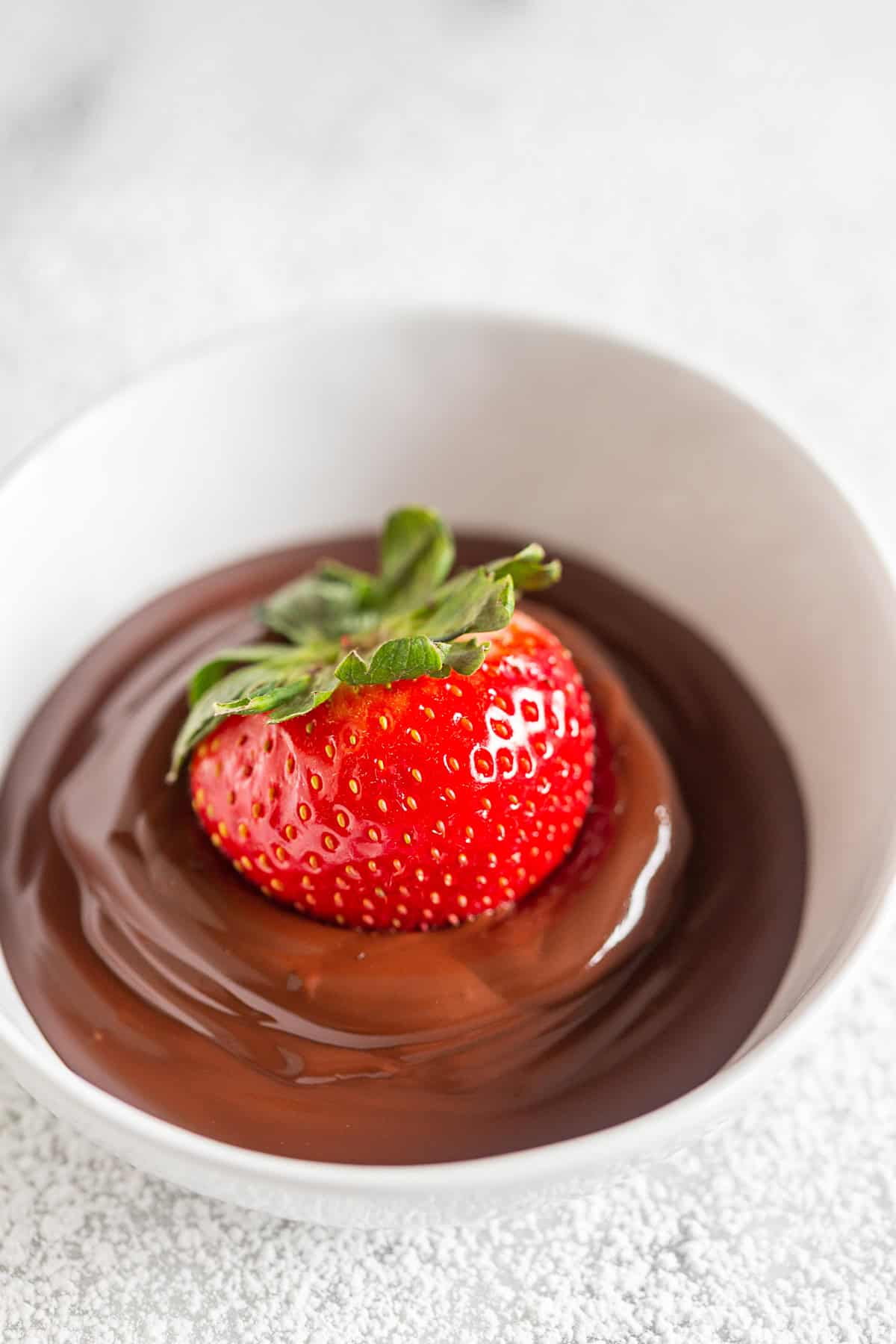 a strawberry sitting in a bow of melted chocolate.