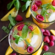 raspberry mango sangria in a glass with fruit around the glasses on a tray