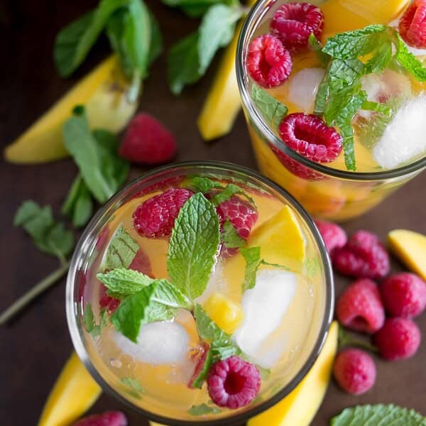 raspberry mango sangria in a glass with fruit around the glasses on a tray