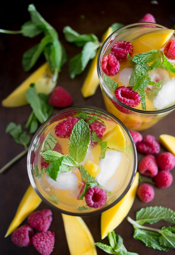 raspberry mango sangria in a glass with fruit around the glasses on a tray