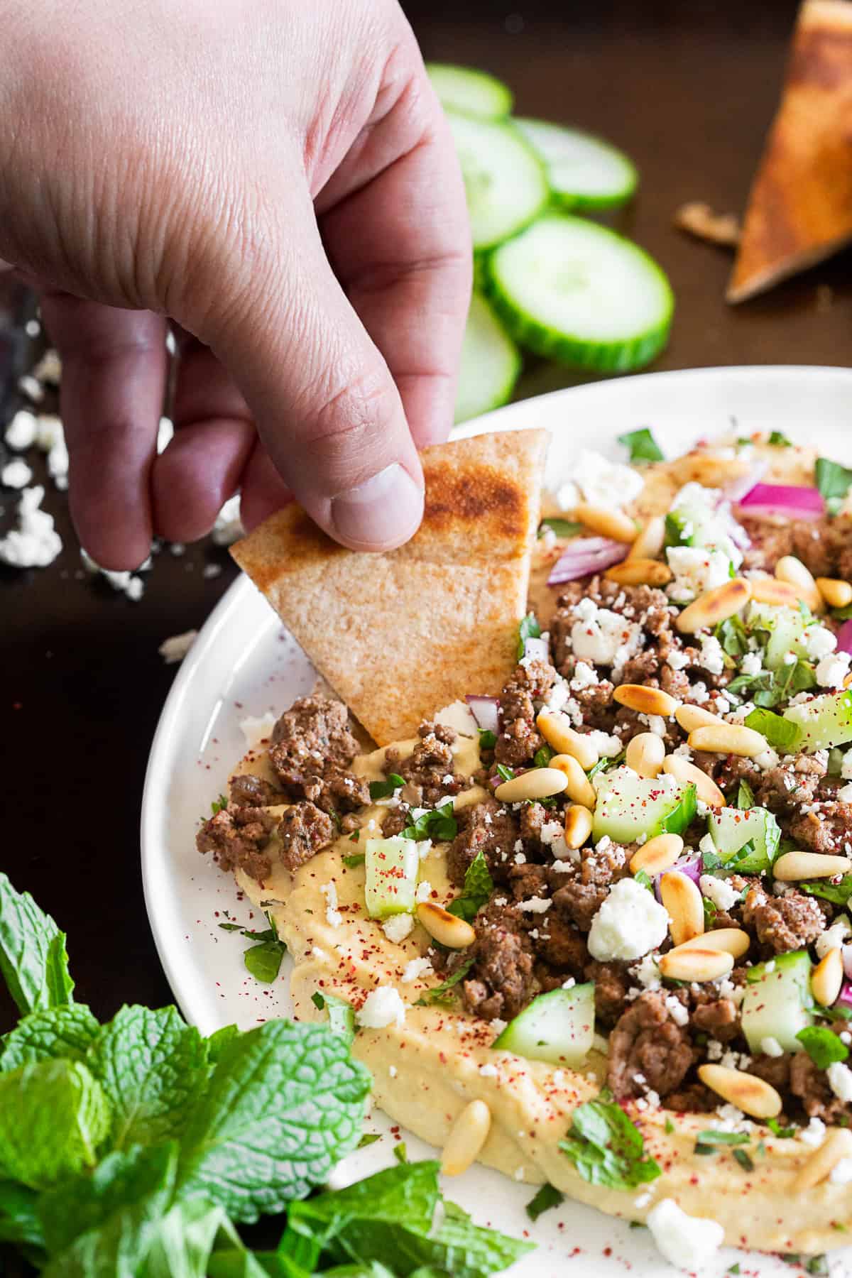 A hand dipping a pita chip into Loaded Greek Hummus. 