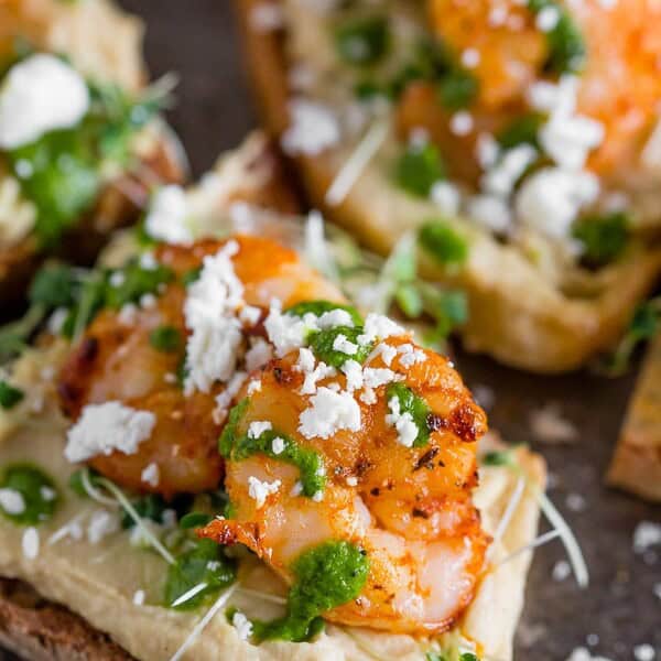 This cajun shrimp hummus crostini is the perfect summer appetizer. Toasted bread topped with hummus, micro greens, spicy cajun shrimp, cilantro pesto and a sprinkling of feta cheese. Hello, summer!