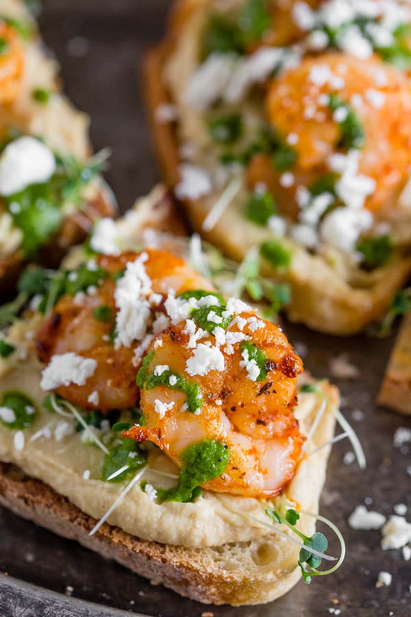 This cajun shrimp hummus crostini is the perfect summer appetizer. Toasted bread topped with hummus, micro greens, spicy cajun shrimp, cilantro pesto and a sprinkling of feta cheese. Hello, summer!