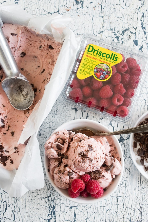 Raspberry Chocolate Chip Ice Cream on a table with a package of a fresh raspberries. 