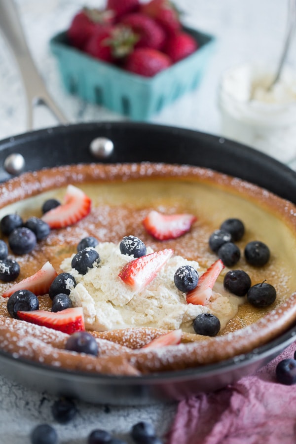 Vanilla Bean Dutch Baby in a skillet topped with berries and whipped mascarpone.