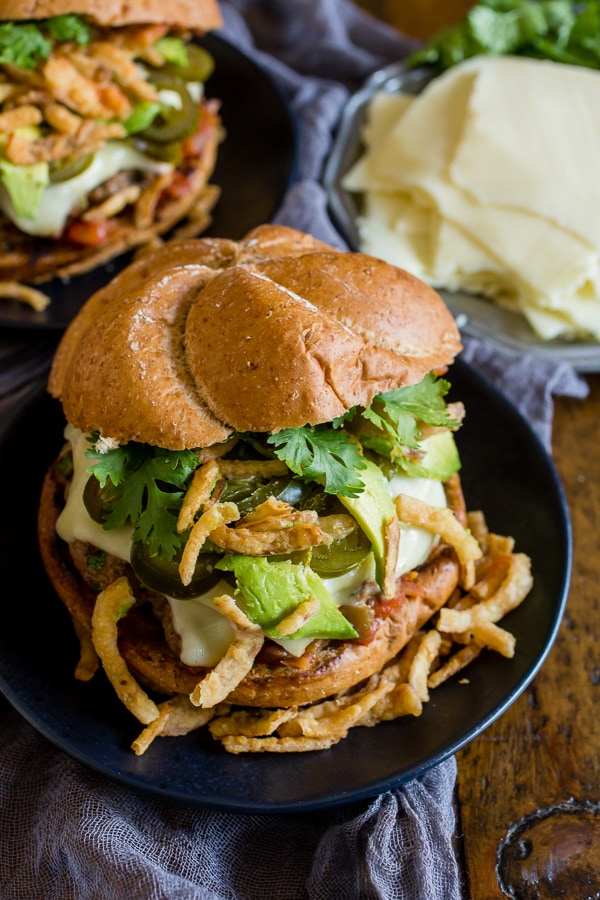 Baja burger on a plate topped with cilantro, crispy onions, and avocado. 