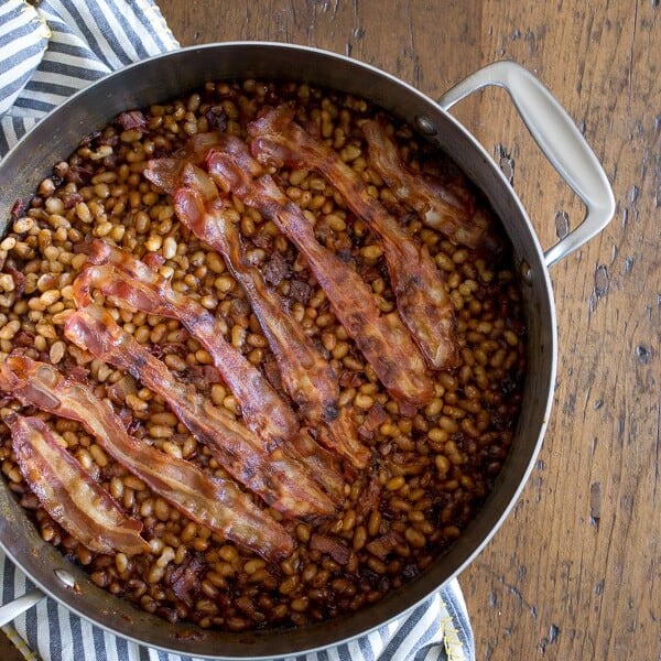 molasses bacon baked beans in a large pan with strips of bacon on top