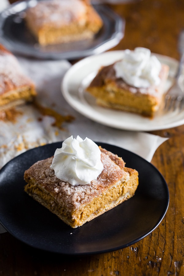 Pumpkin Churro Cheesecake Bars on a plate with whipped cream. 