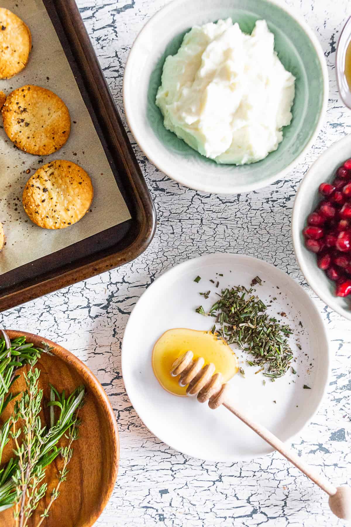 pie crust cracker, whipped goat cheese, honey, rosemary, and pomegranate seeds on a table. 