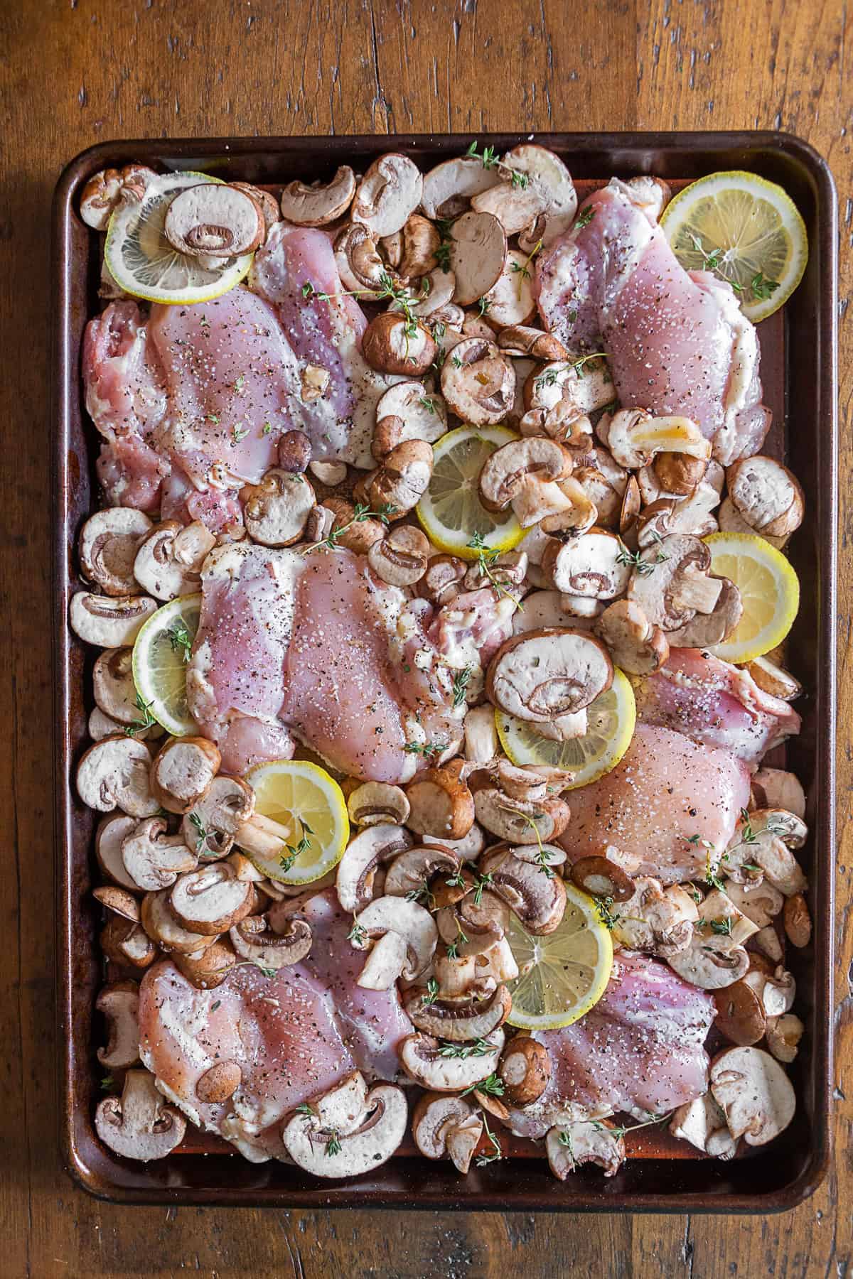 Uncooked ingredients for Sheet Pan Garlic Lemon Chicken on a sheet pan.